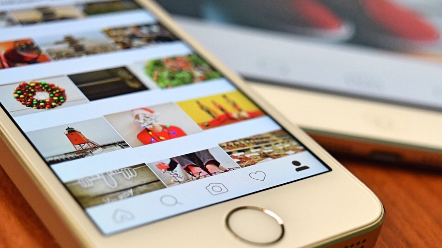 A close-up angled shot of a white smartphone resting on a wooden table, displaying a colorful photo grid on an Instagram user profile.