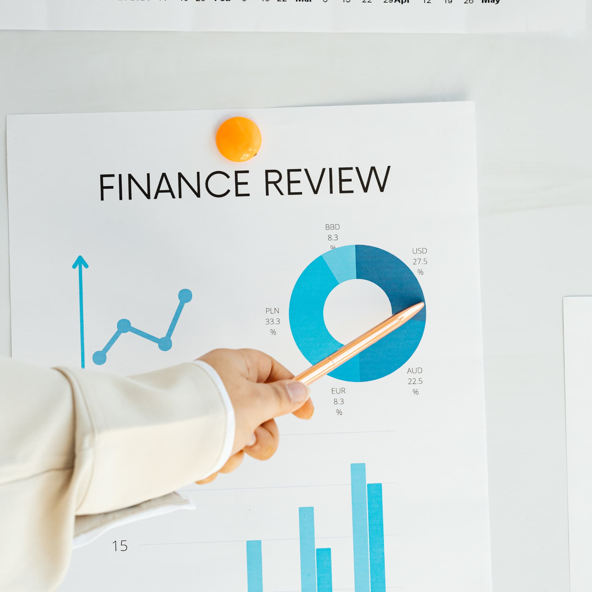 Close-up of a finance report titled “Finance Review” with charts and graphs, as a hand points to a circular chart with a pencil.