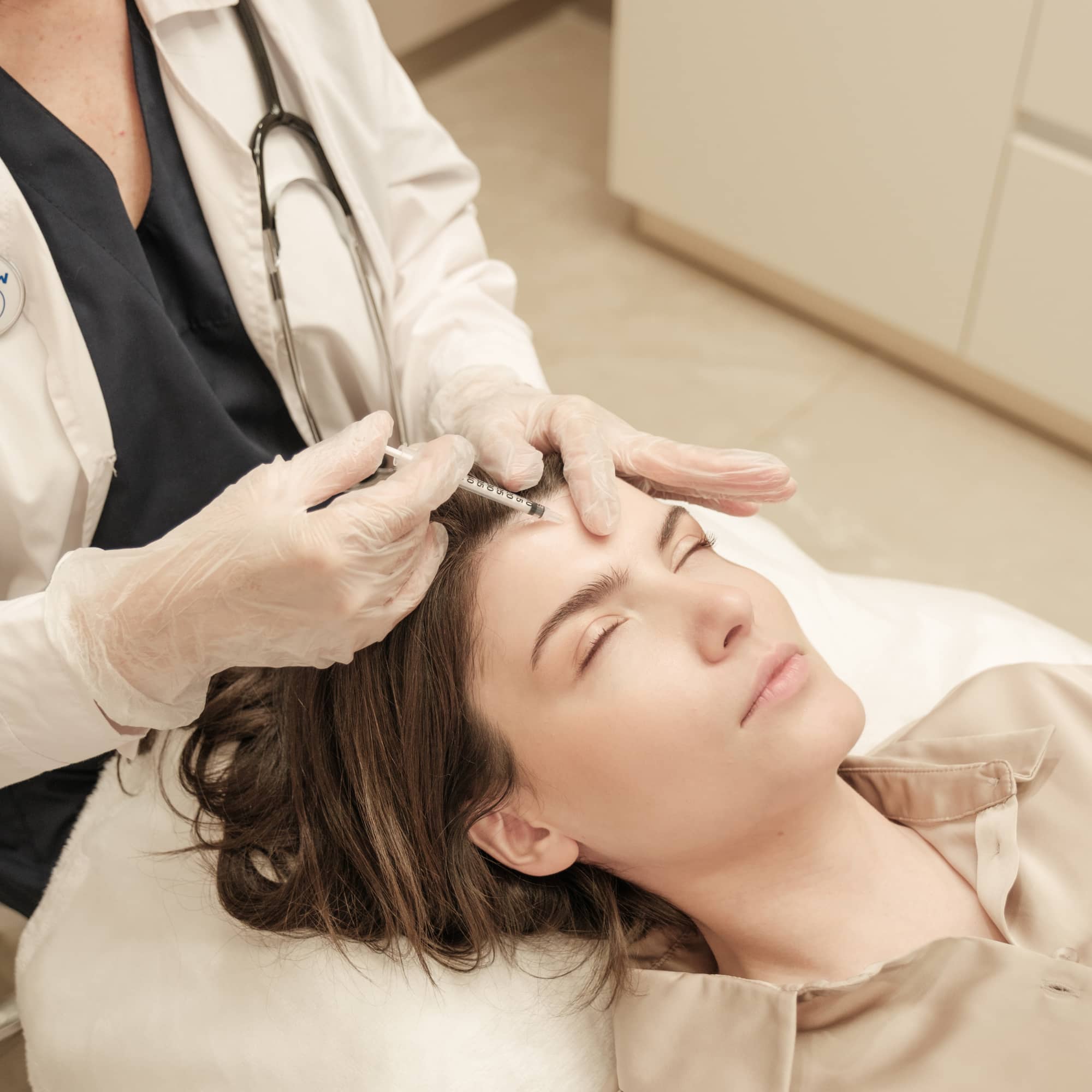 A medical professional administering a forehead injection treatment to a relaxed patient in a clinical setting.