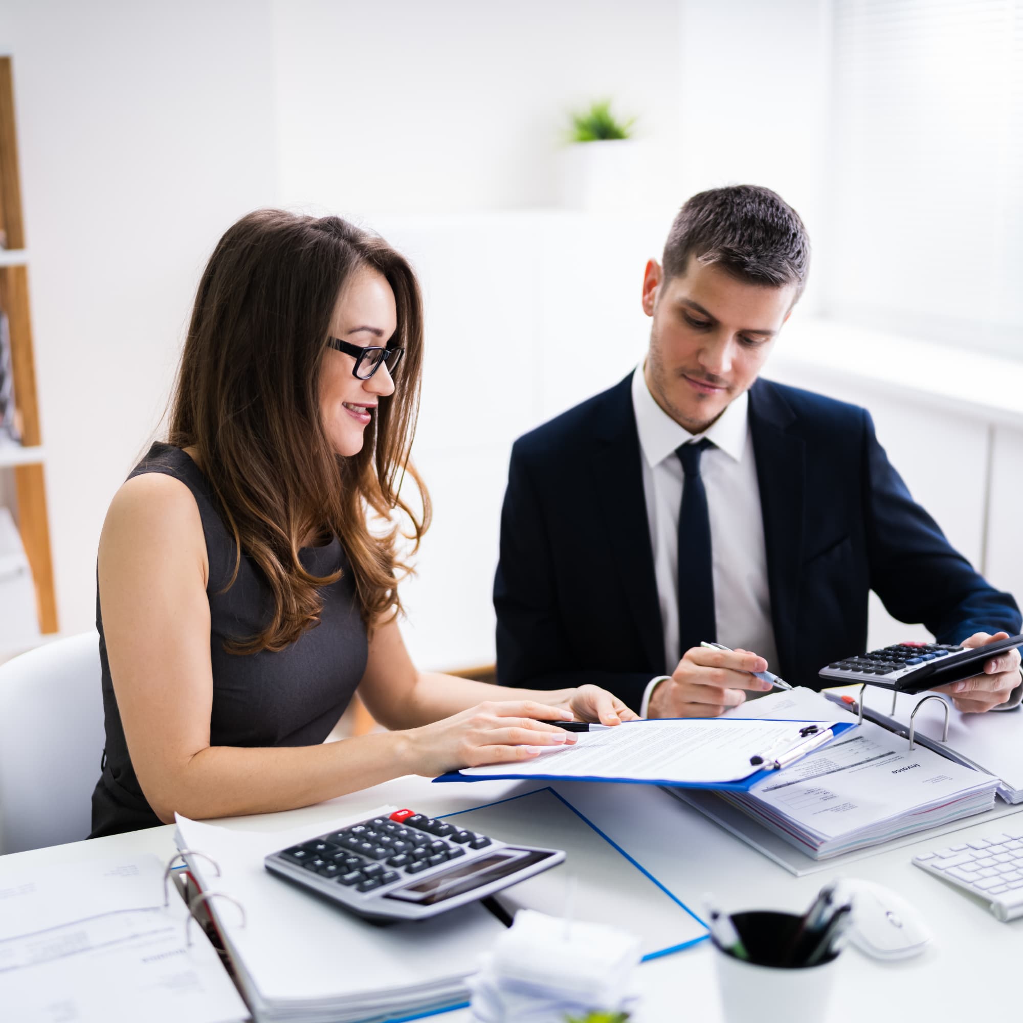 Two professionals reviewing financial documents together, using calculators and paperwork during a budgeting or accounting discussion.