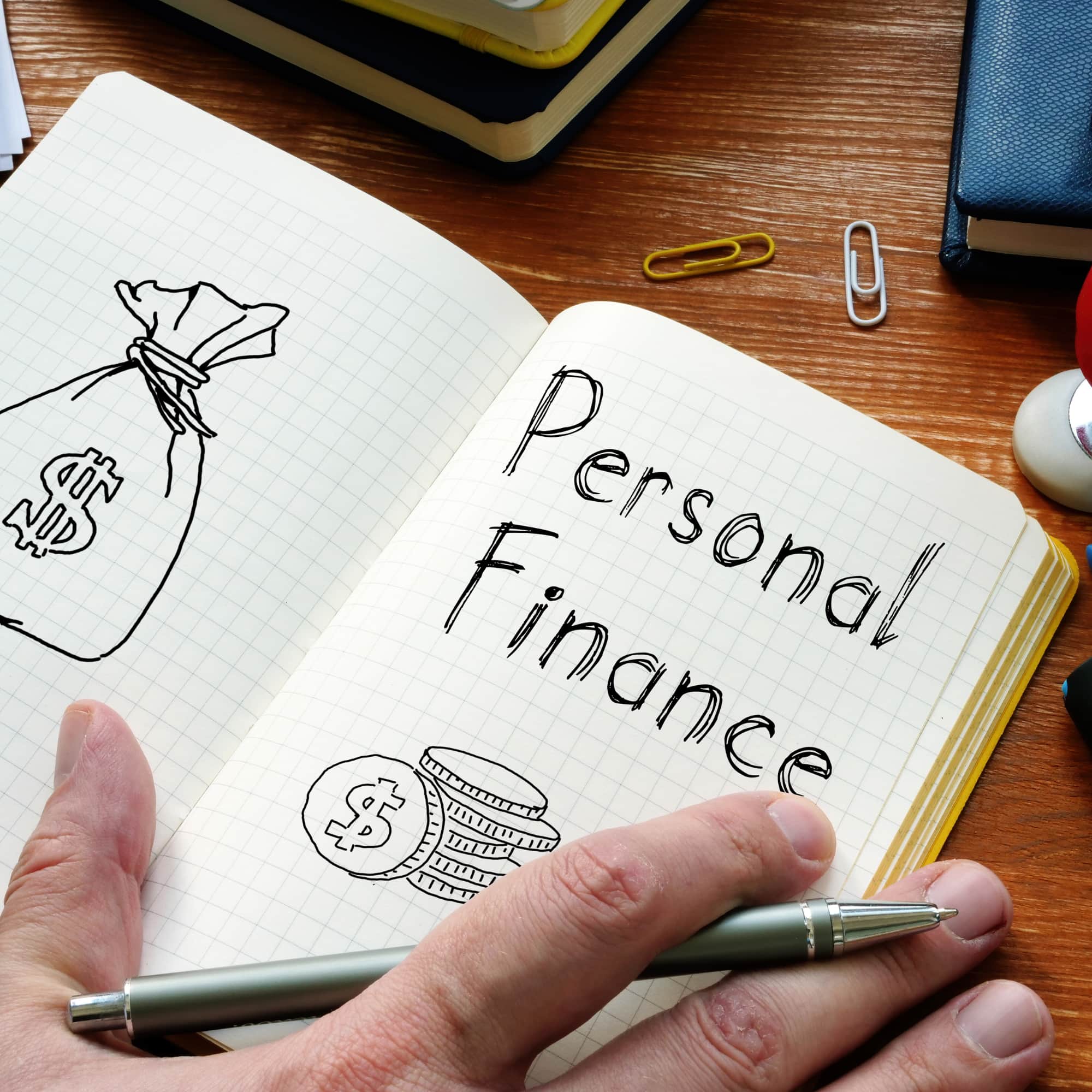 Notebook with “Personal Finance” written on it, featuring hand-drawn money illustrations, coins, and a pen placed on a desk.