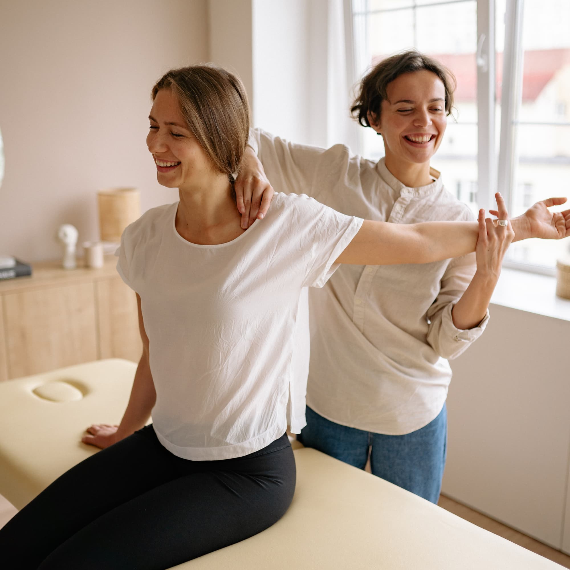 A therapist guiding a woman through a shoulder stretch exercise on a treatment table, focusing on mobility and rehabilitation in a calm clinical setting.