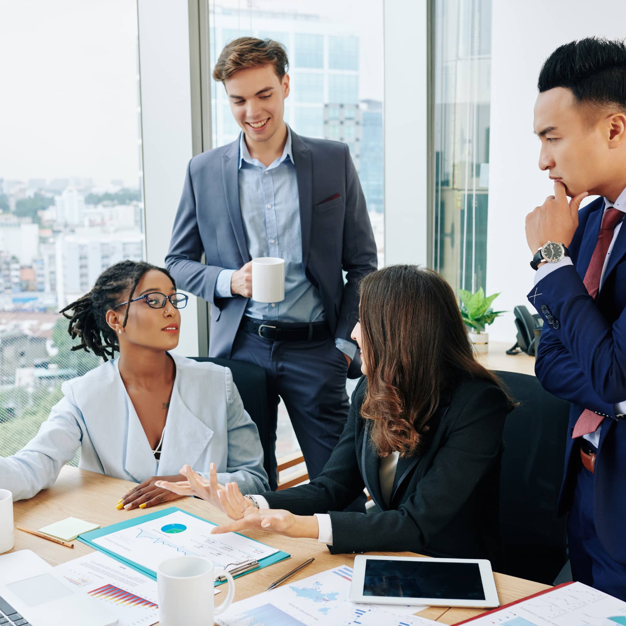 Team of professionals discussing financial reports in an office meeting, reviewing charts and data on a table with a tablet and documents.