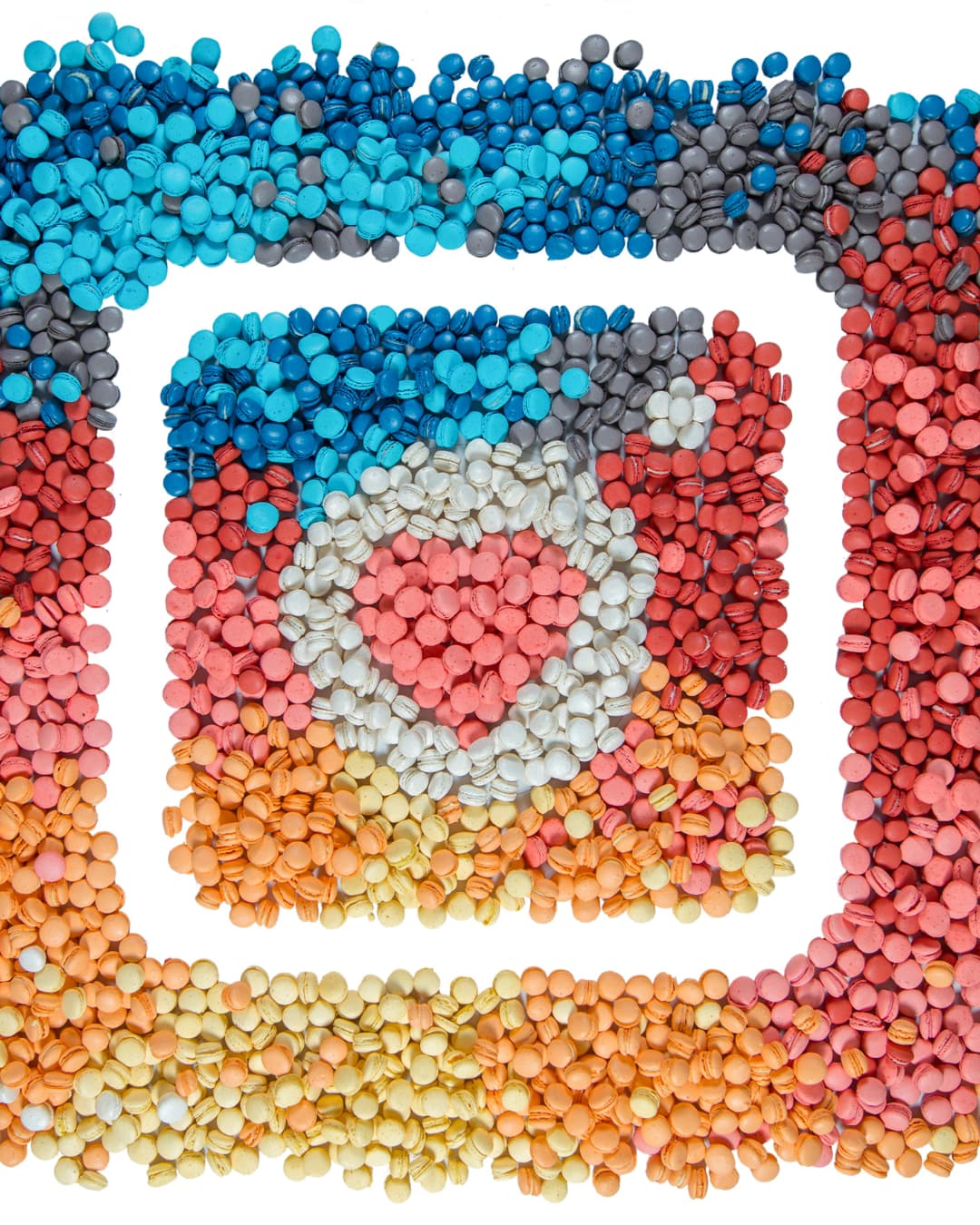 An overhead shot of the Instagram logo intricately recreated using hundreds of colorful mini macarons arranged on a white background, featuring a heart shape in the center camera lens.