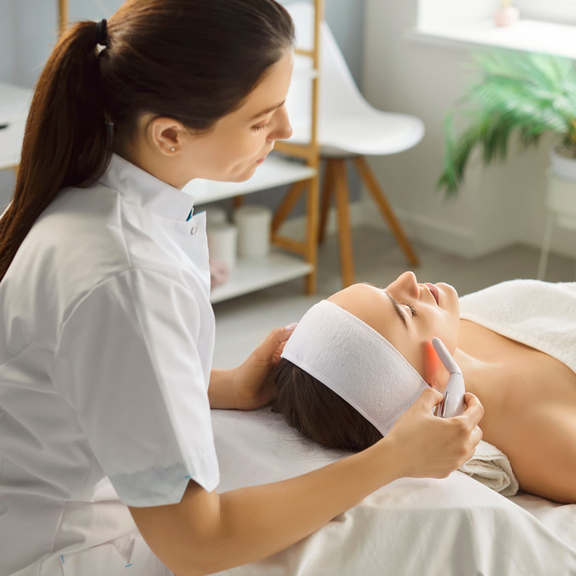 A skincare professional performing a facial treatment on a relaxed client using a handheld device in a clean, modern spa setting.