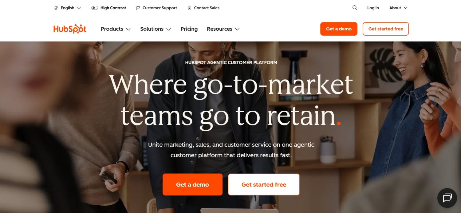 The image displays the HubSpot website homepage, featuring a background photo of smiling professionals in an office and the prominent headline 