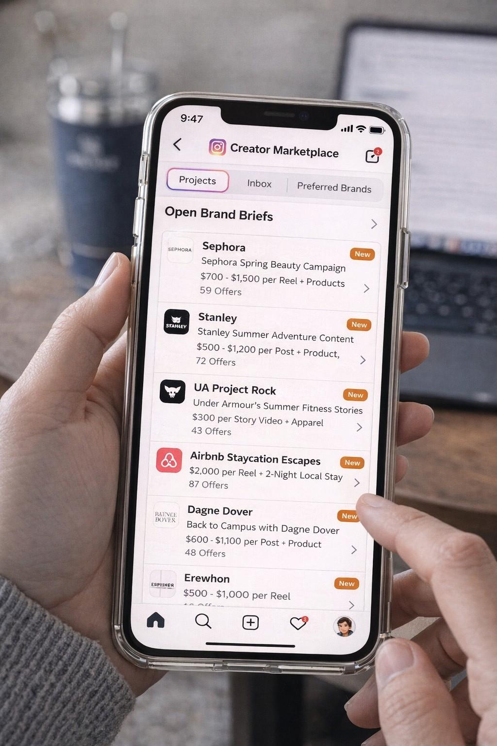 A person holding a smartphone displaying the Instagram Creator Marketplace screen, showing a list of brand matches and sponsorship deals from companies like Nike and Glossier.