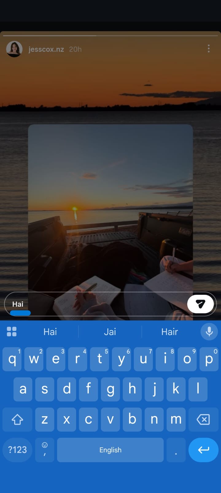 Instagram Story screenshot featuring a sunset over calm water viewed from the back of a pickup truck, where two people are writing in notebooks. The user is replying to the story with the message