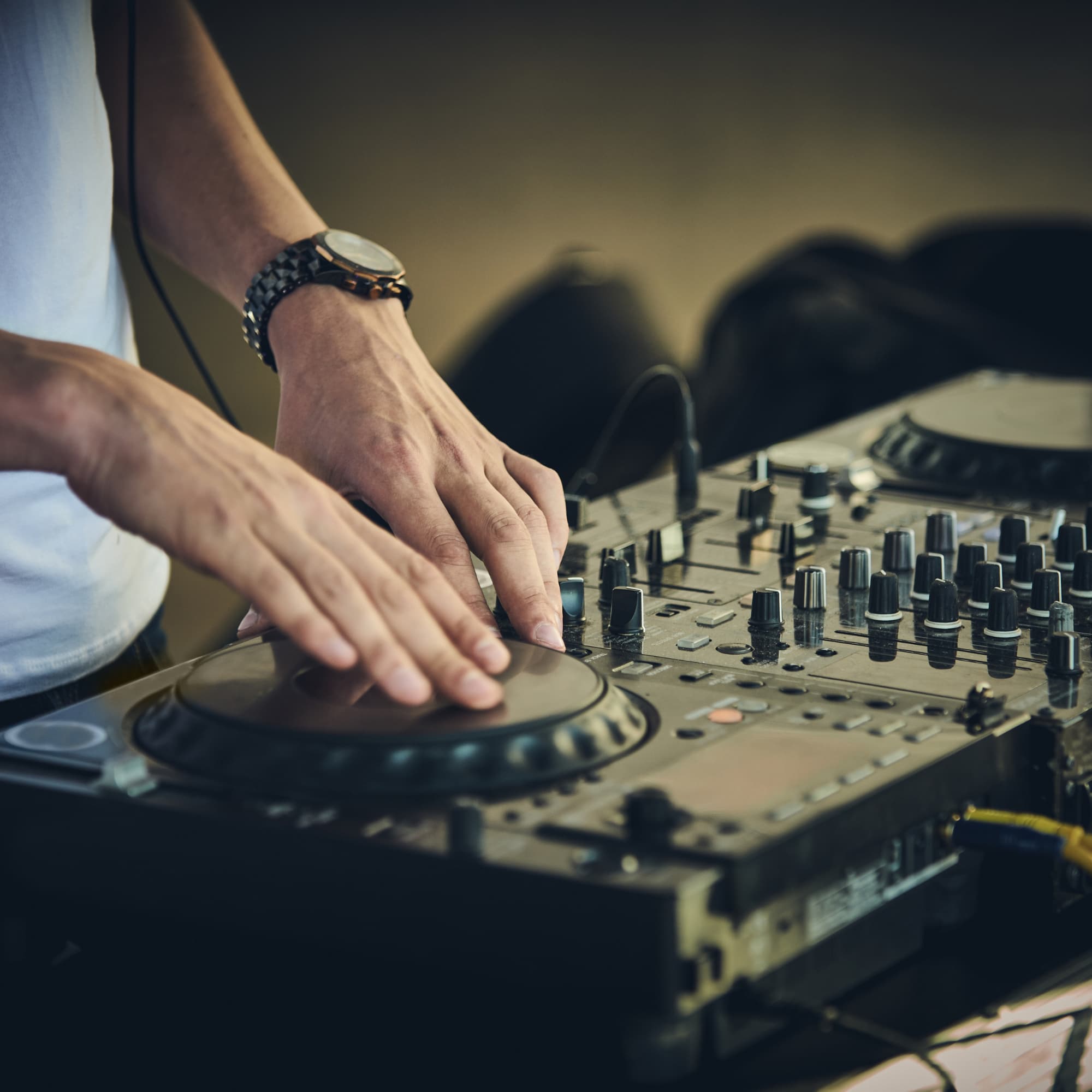 Close-up of a DJ’s hands adjusting controls and scratching on a professional DJ mixer and turntable, with knobs and faders visible.