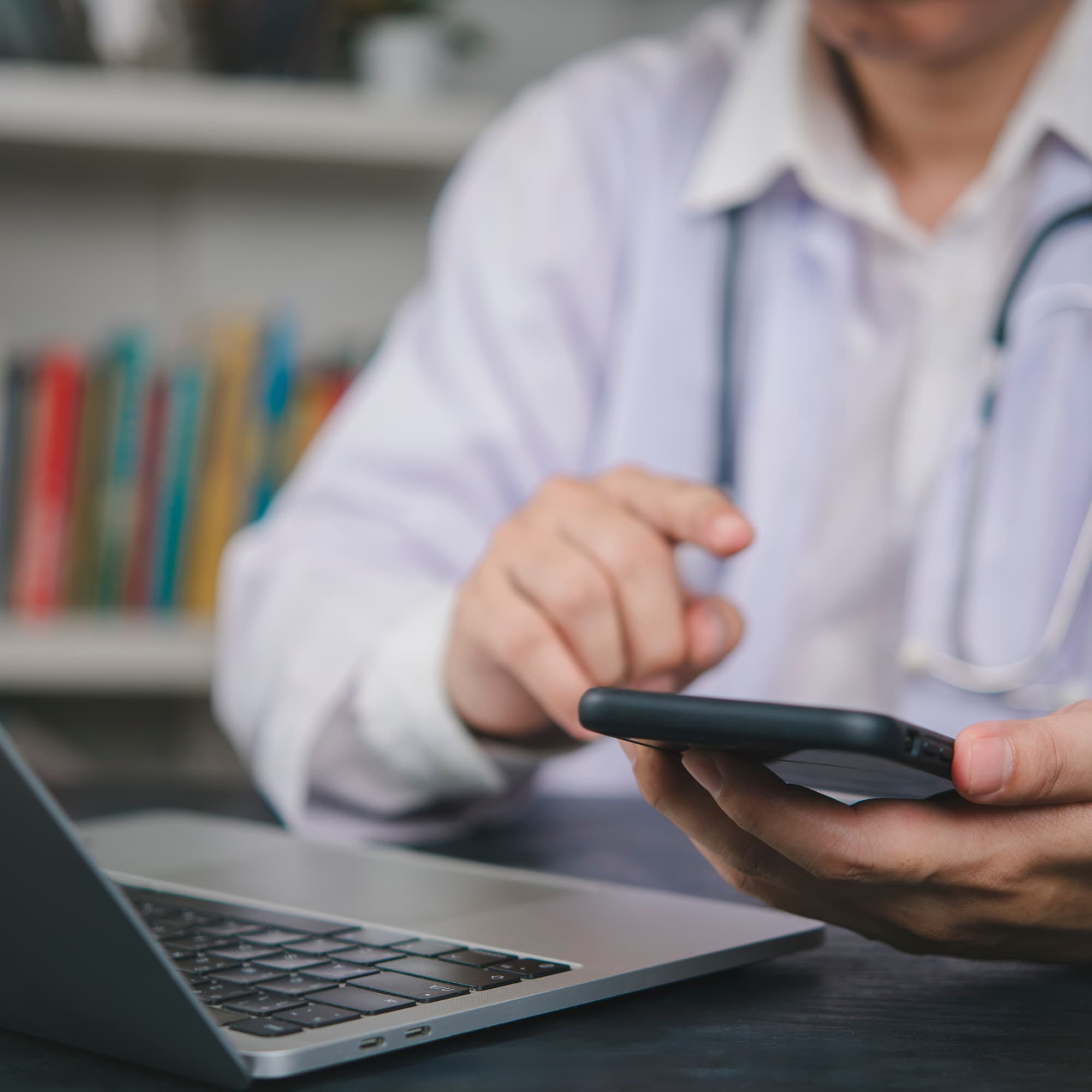 A healthcare professional using a smartphone beside a laptop in a clinic setting, suggesting digital communication or telehealth services.