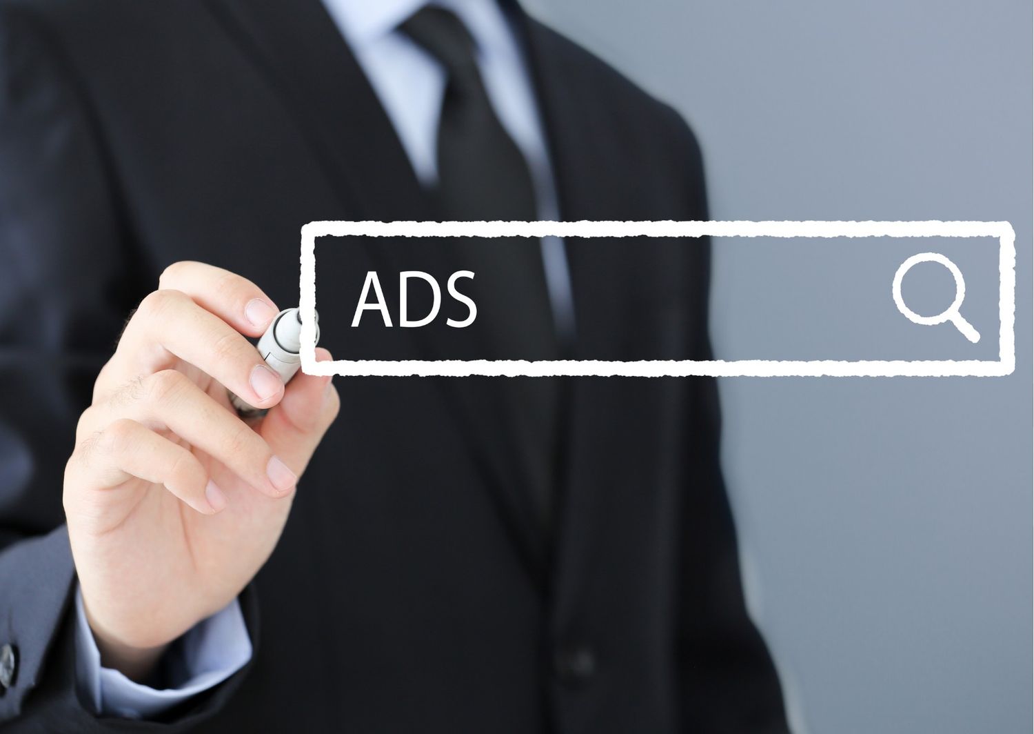 This image shows a person in a professional black suit and tie using a marker to draw or highlight a digital search bar containing the word "ADS." It’s a clean, corporate visual that emphasizes the deliberate nature of setting up and targeting advertising campaigns.