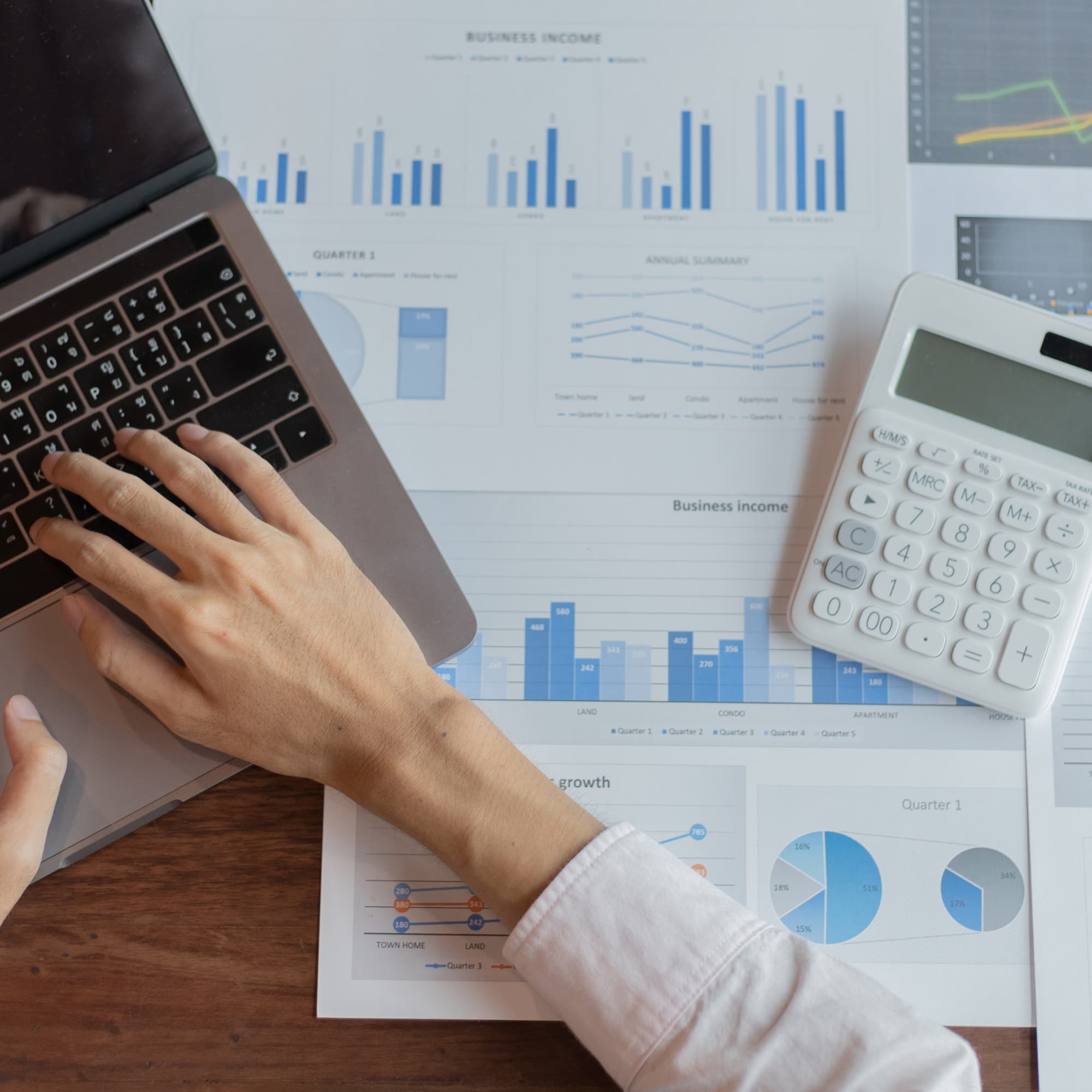 Person analyzing financial data on a laptop with charts and reports, using a calculator to review business income and performance metrics.