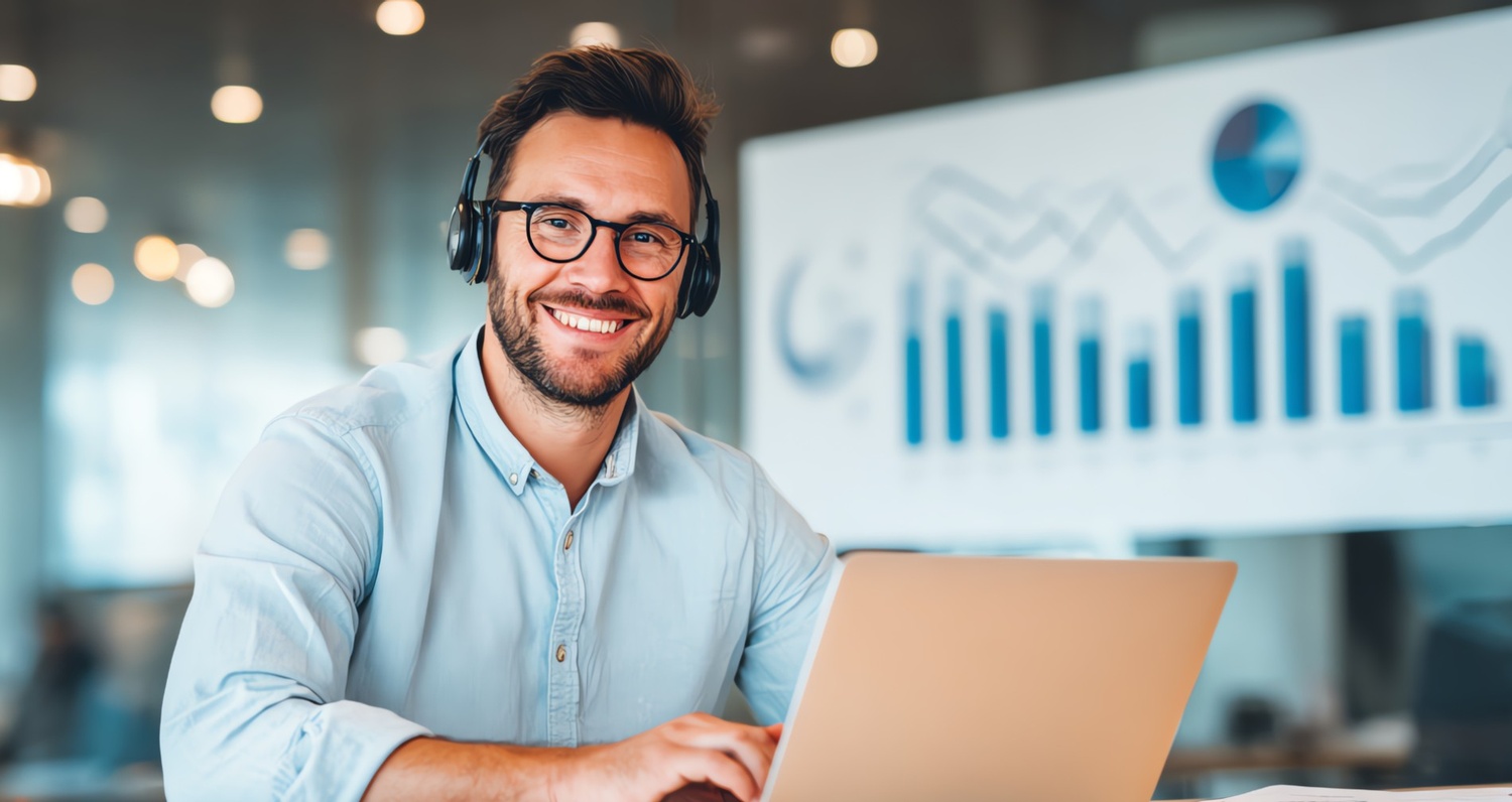A smiling professional wearing a headset and working on a laptop in a modern office, with a blurred data chart in the background, representing the human element in the 2026 algorithm shift toward authentic engagement