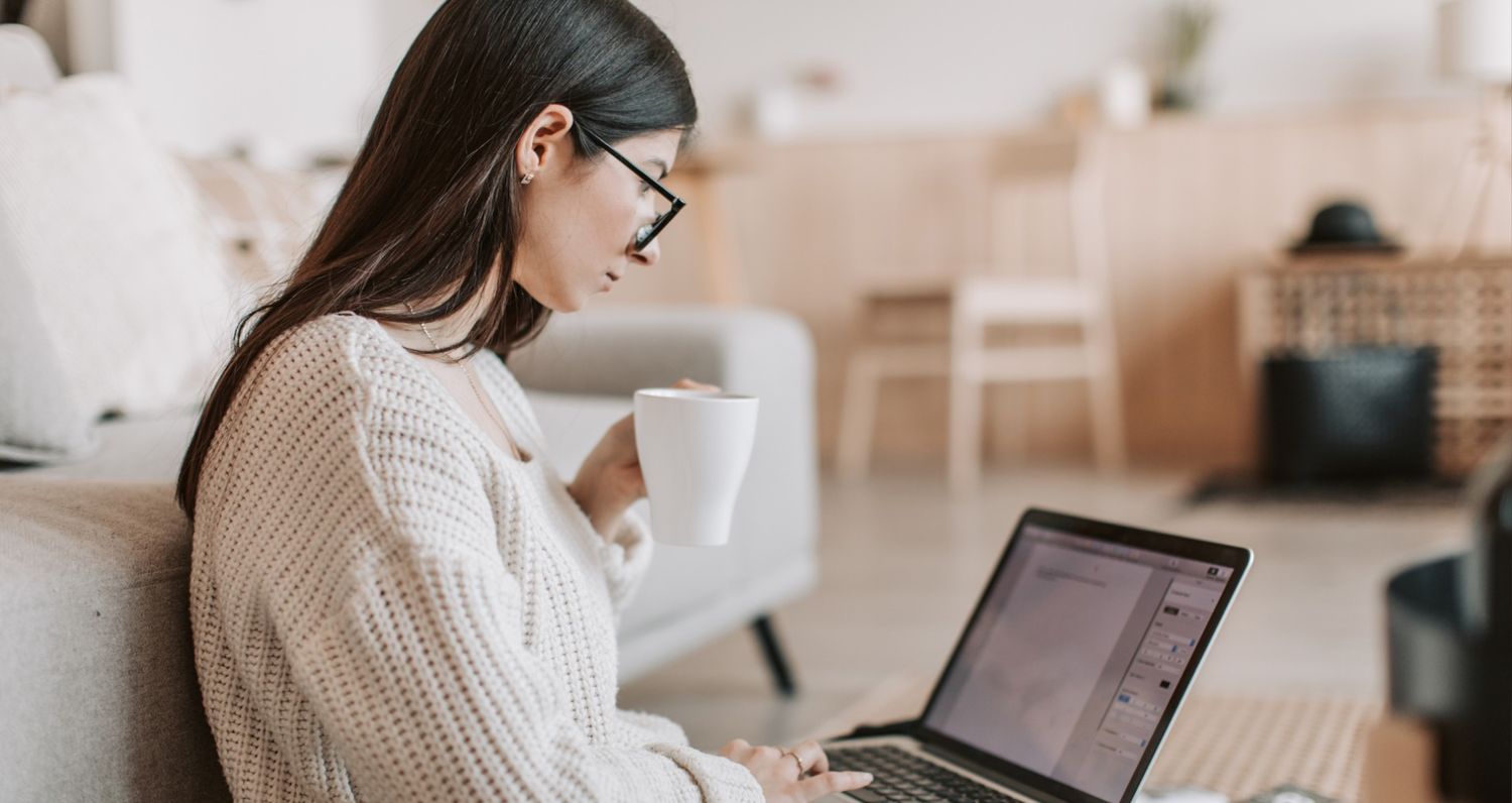 Gemini said
A woman with glasses is sitting on the floor in a bright, modern living room, leaning against a sofa while working on her laptop. She holds a white coffee mug and appears focused on the screen, illustrating a comfortable yet productive "work from home" or content creation lifestyle.