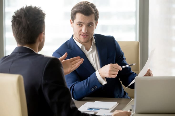Two men in business suits having a meeting and discussing a document at an office desk.