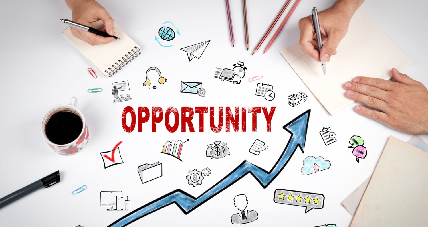 An overhead view of two people working at a desk surrounded by business sketches and a rising blue arrow pointing toward the word "OPPORTUNITY" in bold red text.