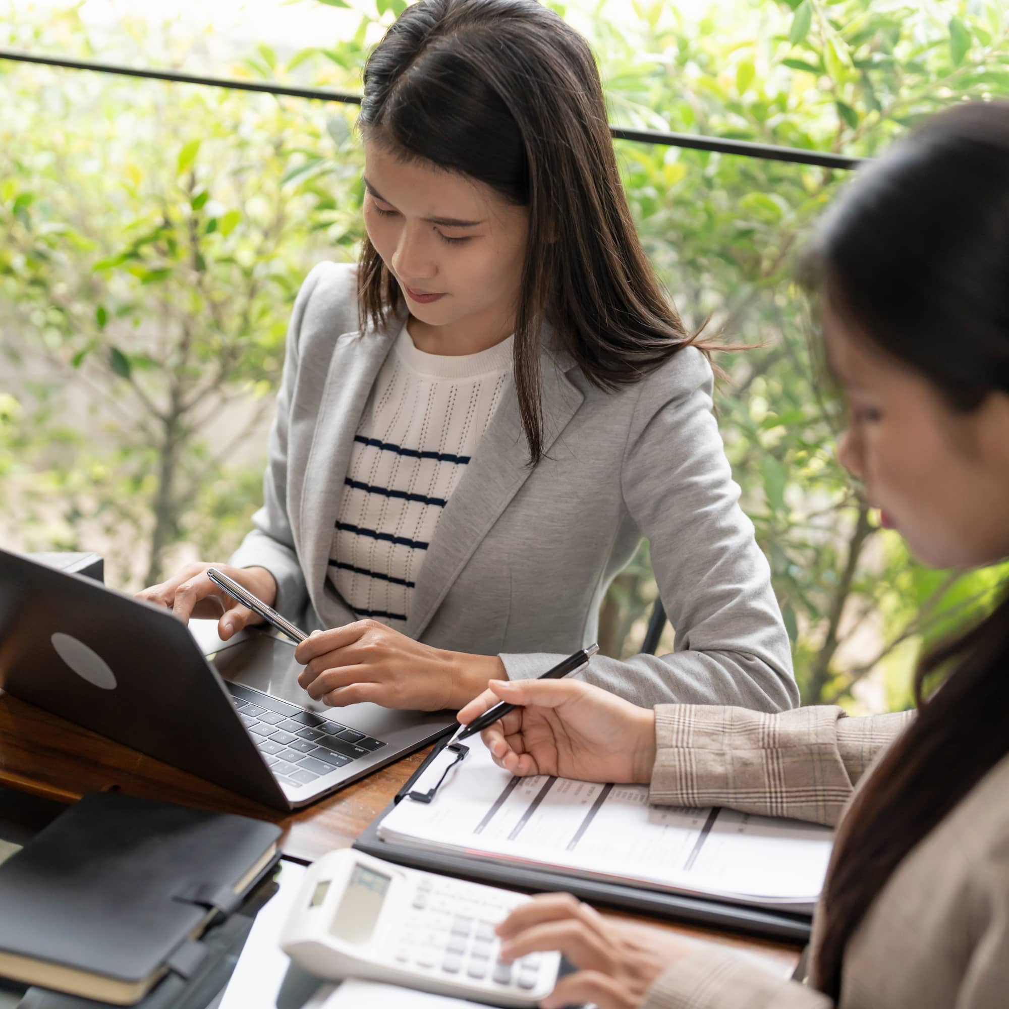 Two professionals working together outdoors, reviewing documents and using a laptop and calculator at a table.