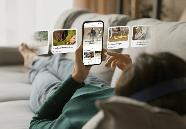 A person lying on a sofa using a smartphone that shows a digital carousel of video thumbnails floating in the air.