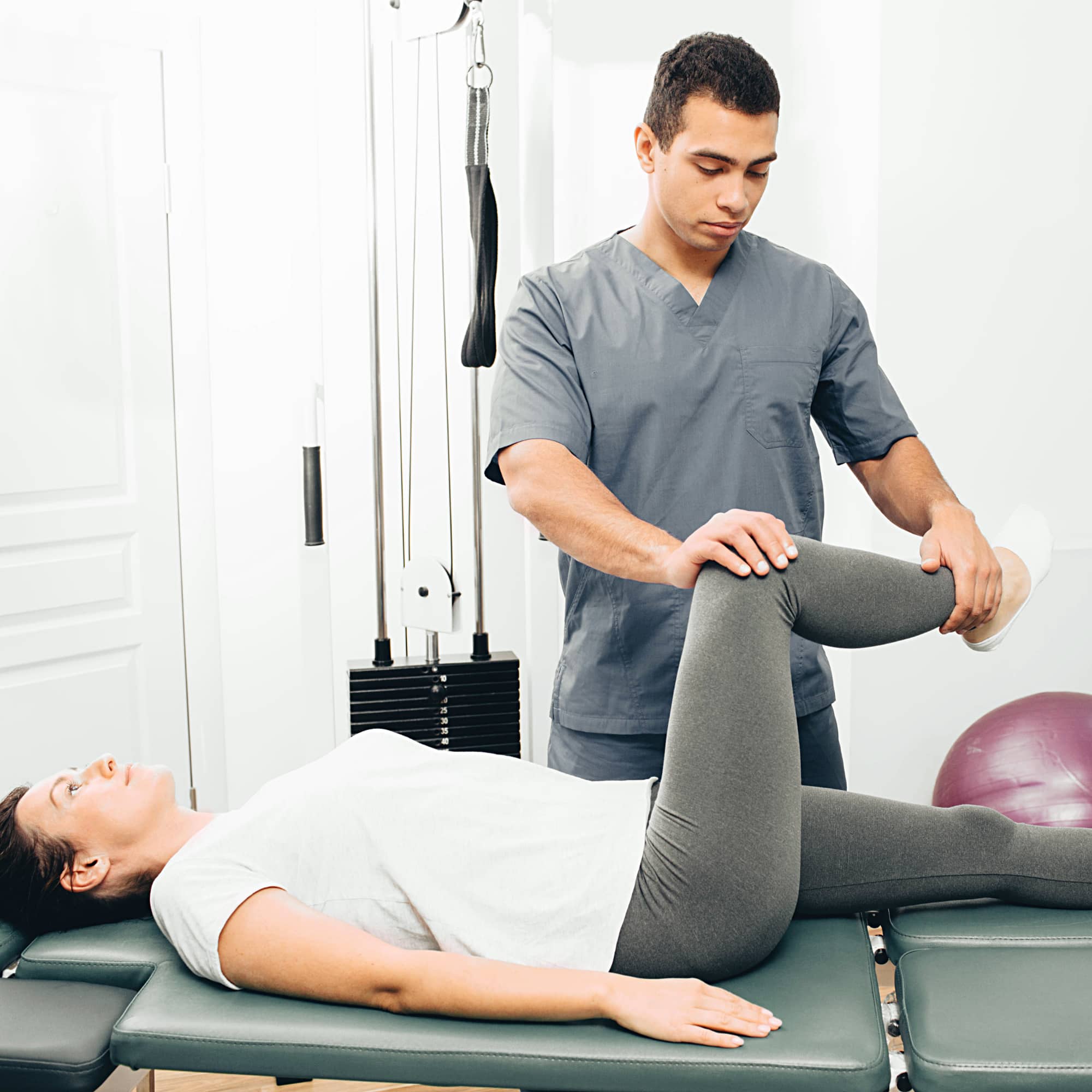 A physical therapist assisting a woman with a leg exercise on a treatment table in a clinical setting, focusing on rehabilitation and mobility improvement.