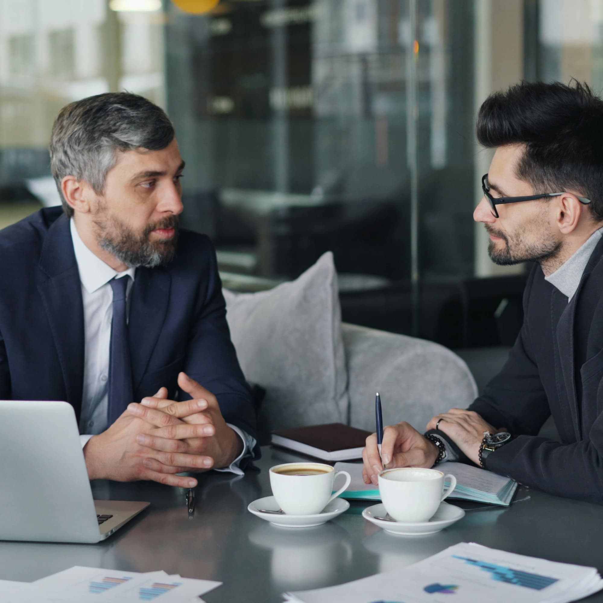 Two business professionals discussing finances at a table, with a laptop, documents, and coffee cups during a meeting.